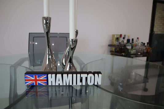 F1 Driver Name Plate with bold lettering 'Hamilton' and UK flag design on modern glass table.