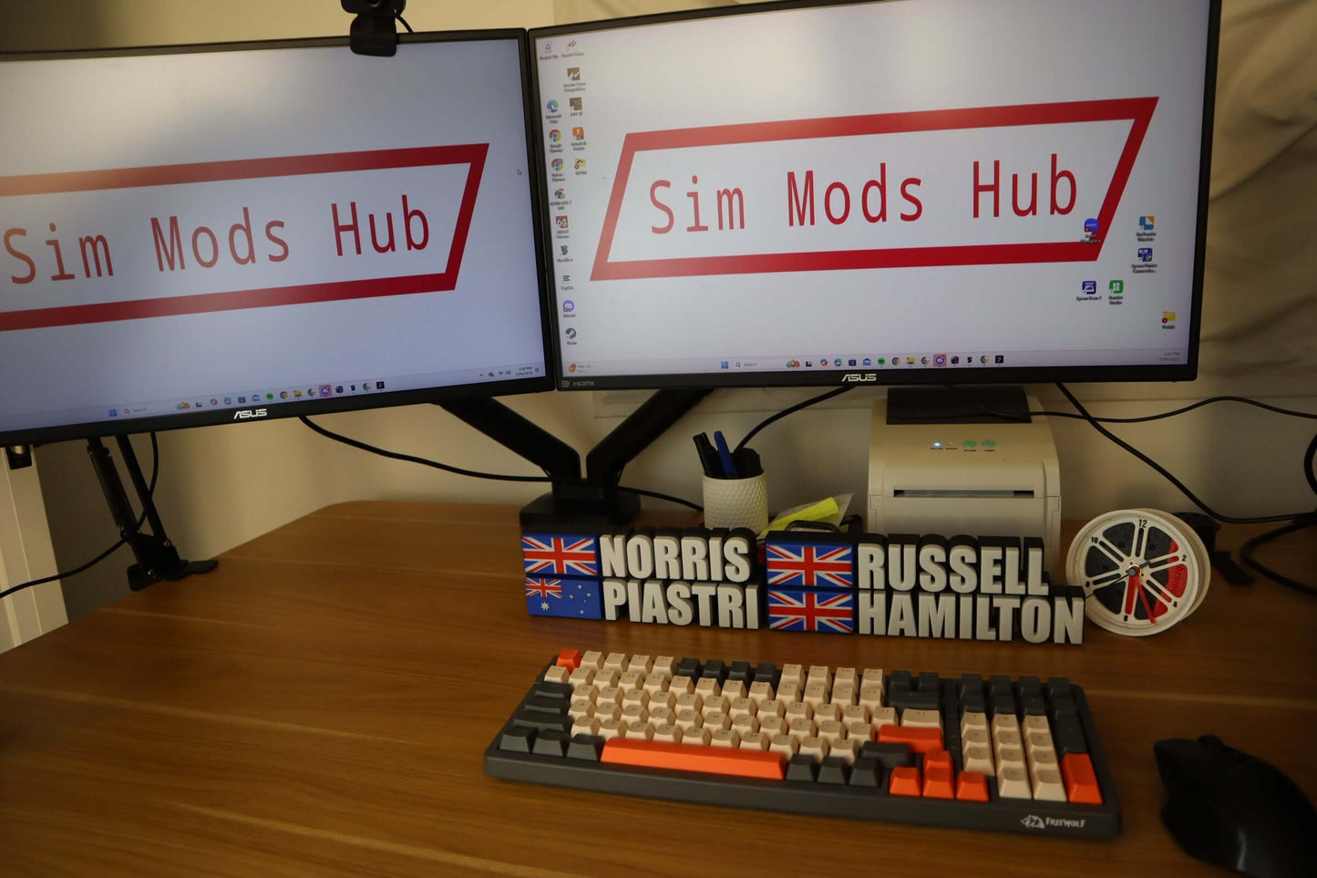 Custom driver name plates for Norris, Piastri, and Hamilton displayed on a desk with a gaming keyboard and dual monitors.
